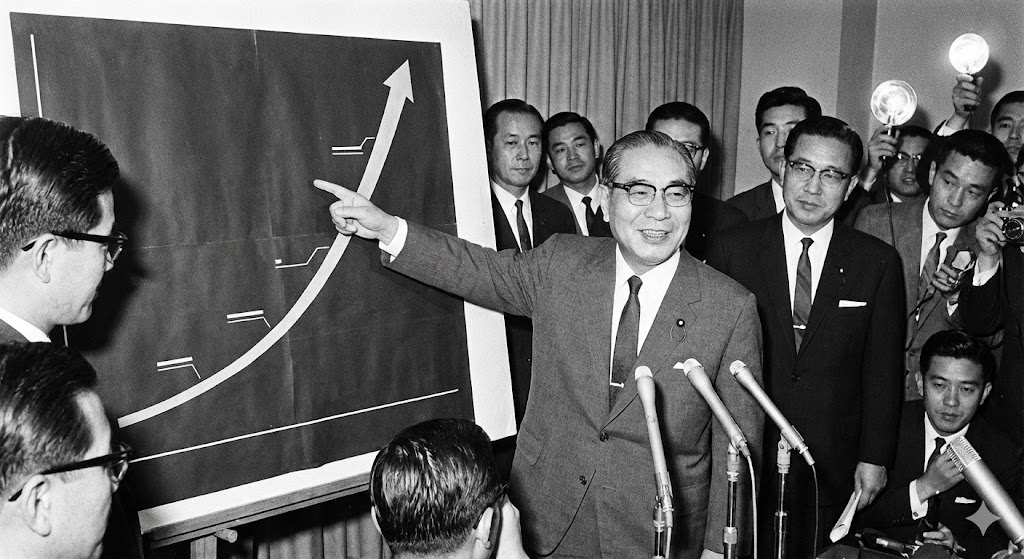 右肩上がりのグラフを指差して自信満々に説明する池田勇人の様子